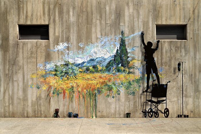 Silhouette of a person painting colorful street art depicting a landscape on a large concrete wall outdoors.