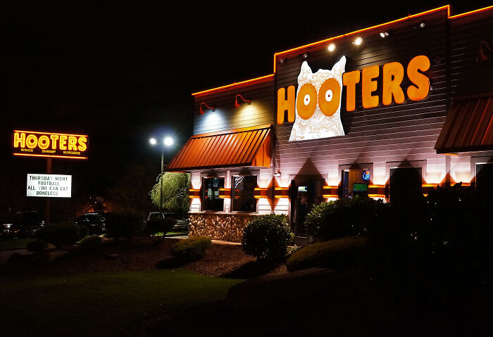 Hooters restaurant at night with bright orange signage, highlighting restaurant workers handling unusual orders.