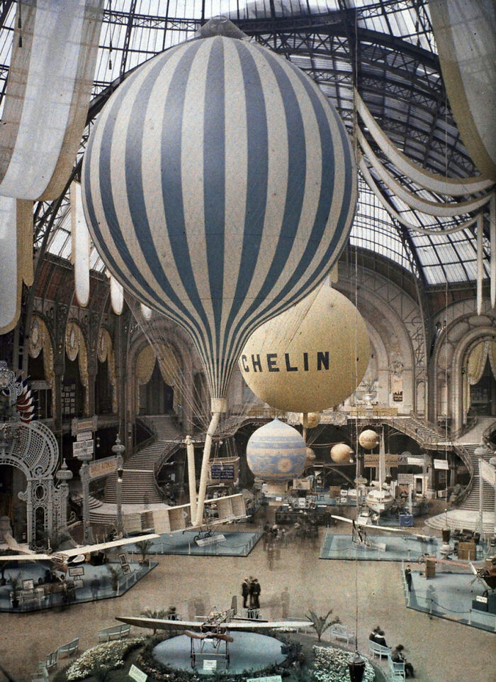 Early 20th century exhibition hall with large balloons and vintage airplanes showcasing important historical achievements.
