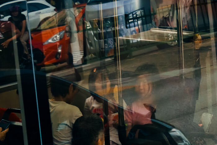 Reflection of people inside a bus creating a poetic, cinematic scene that captures ordinary moments through photography.