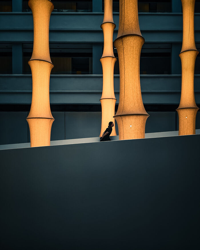 Photographer capturing poetic cinematic image of person walking near large glowing architectural columns at night.