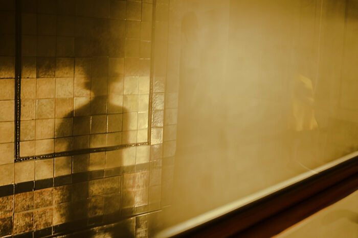 Shadowy silhouette of a person reflected on a tiled wall creating a poetic, cinematic moment by a skilled photographer.