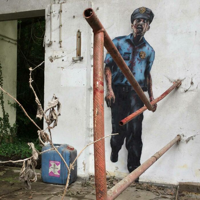 Graffiti art of a police officer interacting with rusted pipes on an old white wall, enhancing urban street surroundings.