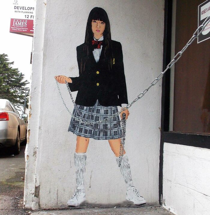 Graffiti art of a girl holding a real chain, creatively making street art interact with the surroundings.