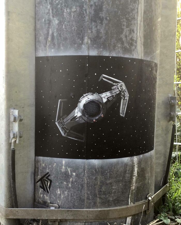 Graffiti art incorporating a vent into a space scene on a street utility pole, creatively interacting with the surroundings.