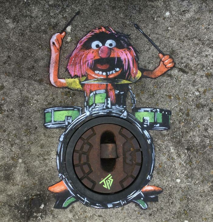 Graffiti of a drummer character interacting with a street manhole, creatively blending art and surroundings.