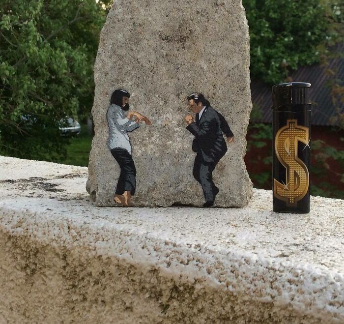 Graffiti art on stone showing two dancing figures interacting with a nearby dollar sign lighter on a concrete surface.