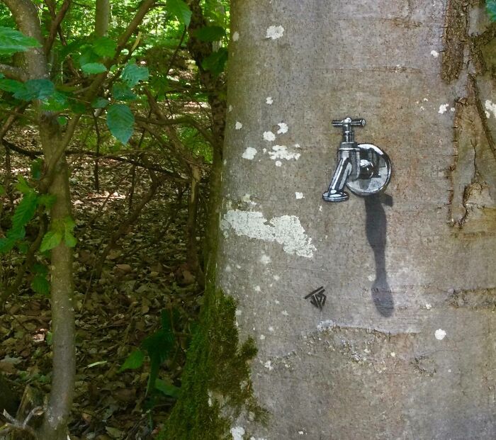 Graffiti artist creates interactive street art of a water faucet painted on a tree blending with natural surroundings.