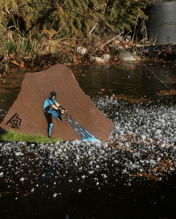 Graffiti art on rock shows a person kicking water droplets that blend with surrounding water and foam outdoors.