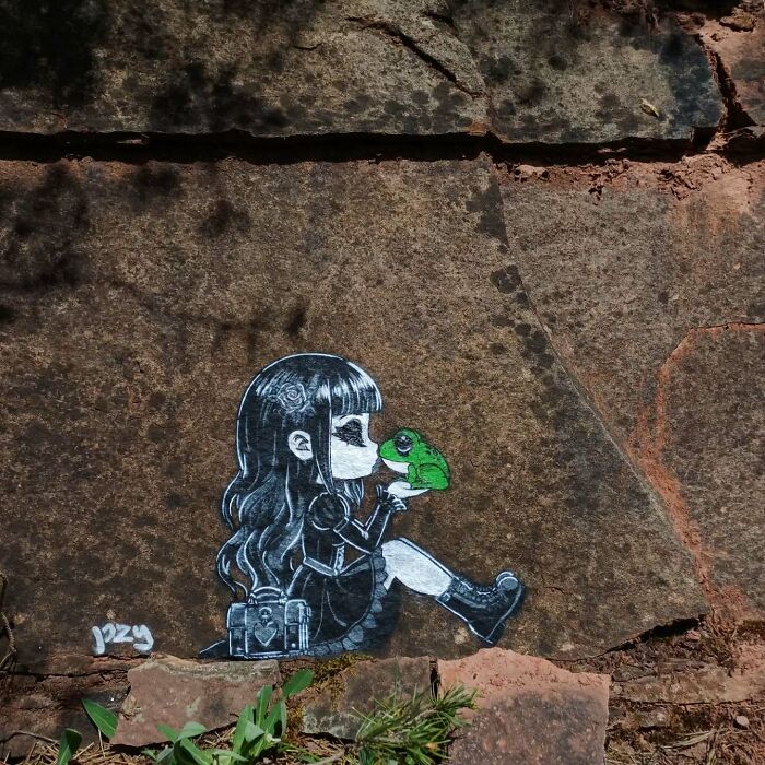 Street graffiti art of a girl holding a green frog, creatively interacting with the natural surroundings on stone surface.