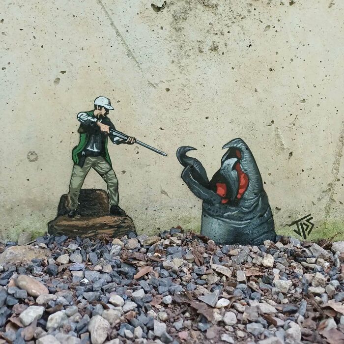 Graffiti art of a man aiming a gun at a giant crab claw emerging from gravel on a weathered concrete wall.