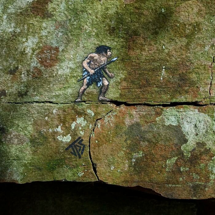 Cave man graffiti art interacting with c*****d rock surface, making streets less boring with creative street art.
