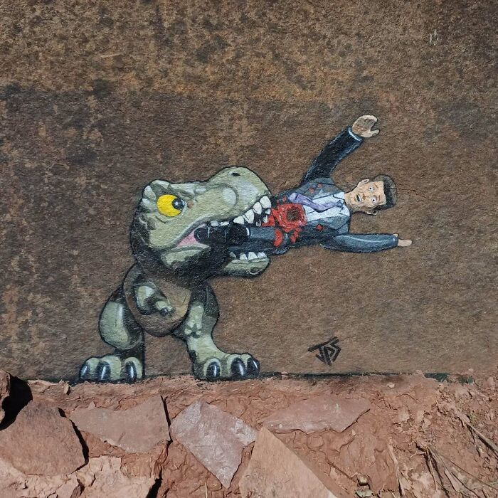 Graffiti of a dinosaur biting a man, creatively interacting with the rough stone surface and surrounding rocks.