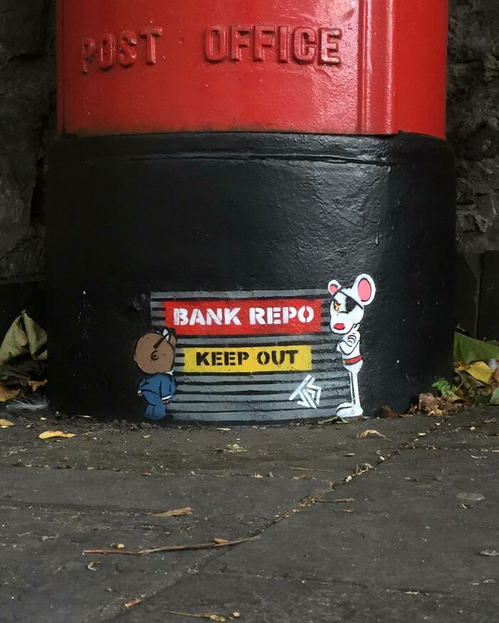 Street graffiti interacting with surroundings depicting characters and a bank repo warning on a painted post office base.