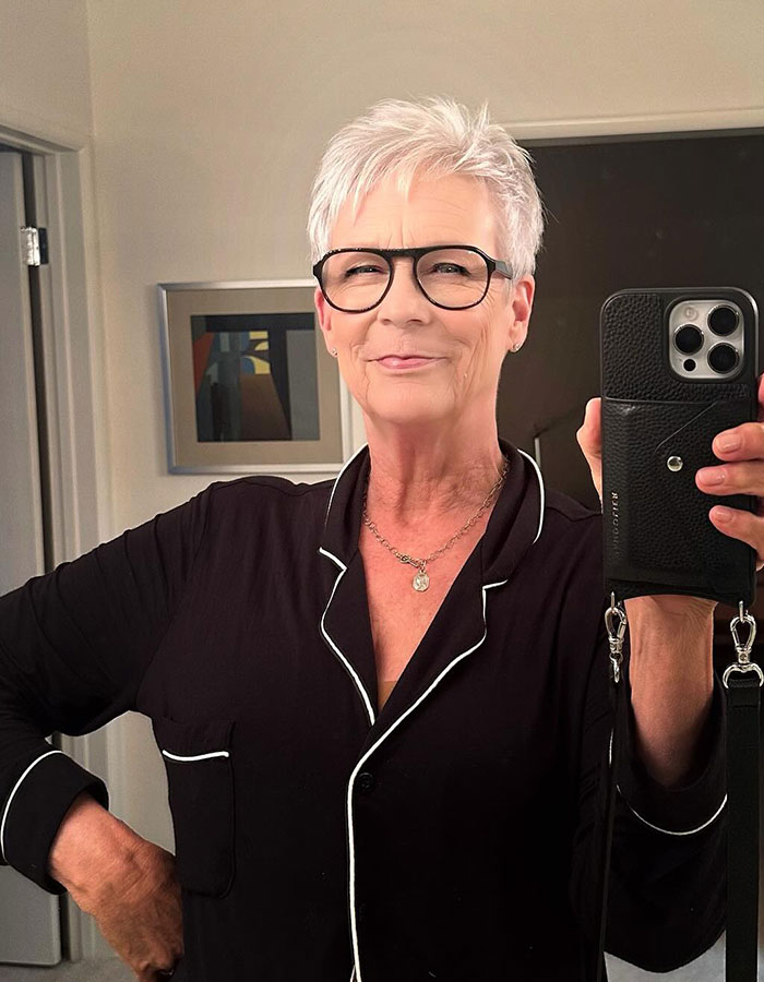 Jamie Lee Curtis taking a selfie wearing glasses and black pajamas, responding to viral fan memes about her cleavage moment.
