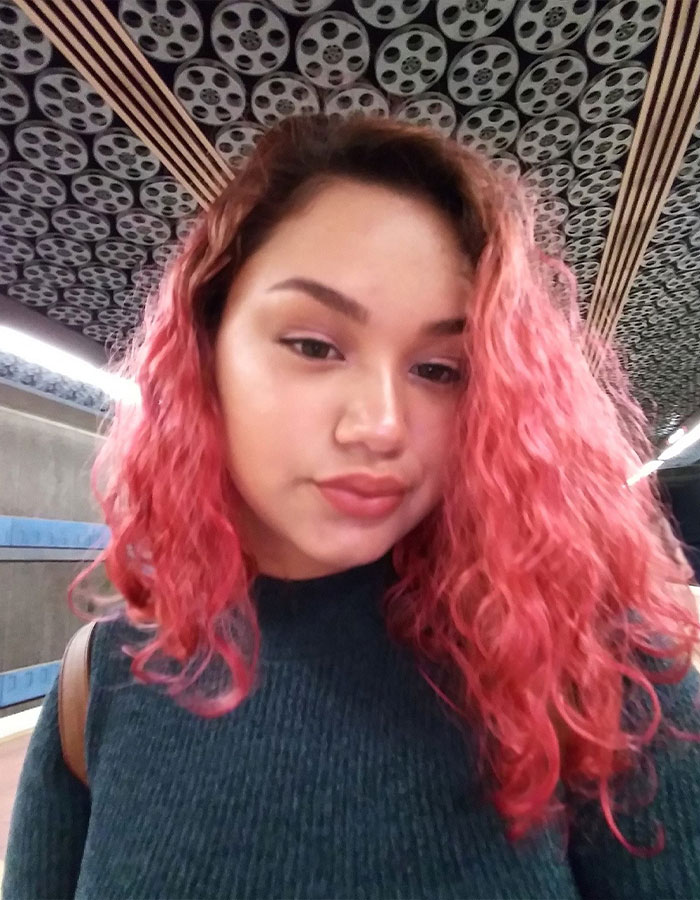 Young woman with pink curly hair wearing a dark sweater in a subway station, related to 7-Eleven manager roommate story.