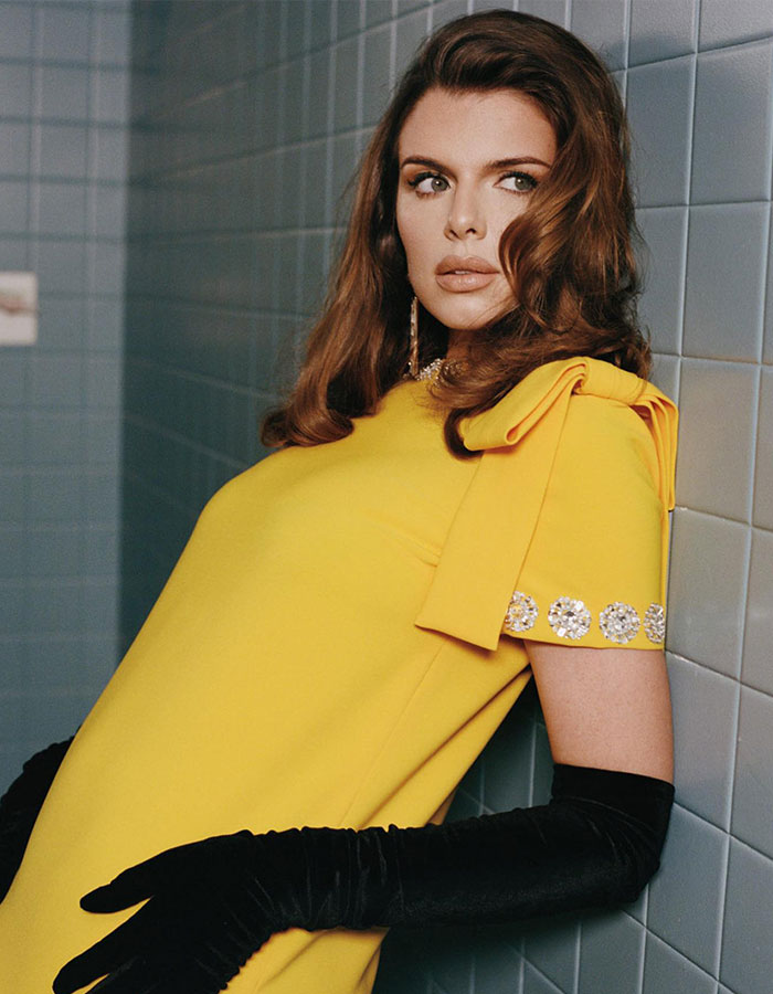 Julia Fox posing in a yellow dress and black gloves, reflecting on her plastic surgeries and public reactions.