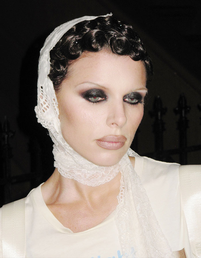 Julia Fox with dramatic eye makeup and vintage lace headscarf discussing plastic surgeries and public reaction.