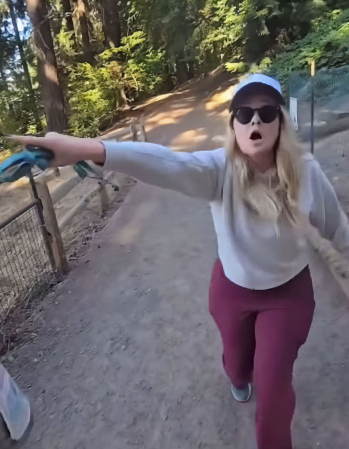Woman angrily confronting man walking dog in wooded park, pointing and yelling during heated harassment dispute caught on camera