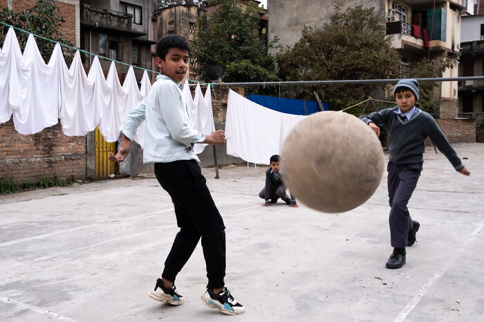Boys playing soccer in a courtyard, captured by street photographer highlighting the beauty of ordinary life.