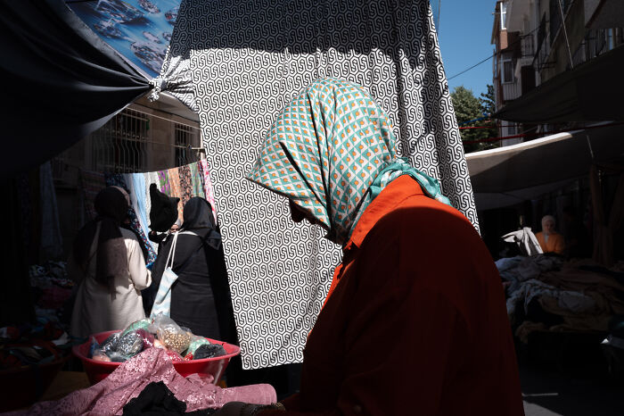 Street photographer captures a woman in a patterned headscarf shopping at an outdoor market, highlighting ordinary life moments.