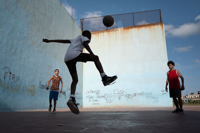 Three boys playing soccer against a graffitied wall, capturing the beauty of ordinary life in street photography.
