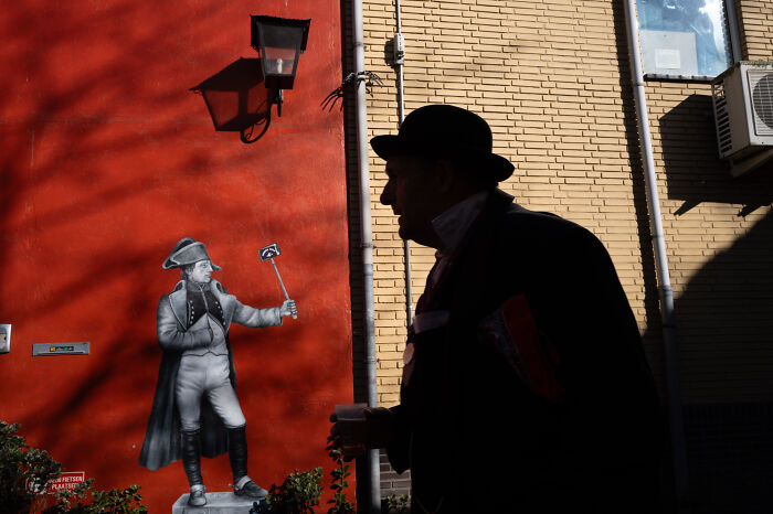 Silhouette of man with hat walking past street art capturing the beauty of ordinary life in an urban setting.