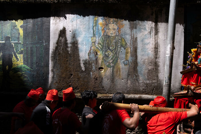Street photographer captures vibrant scene of people in red hats carrying a wooden beam against a mural backdrop.