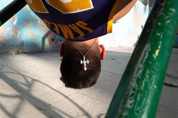 Young man hanging upside down on green bars, street photographer capturing the beauty of ordinary life in a candid moment.