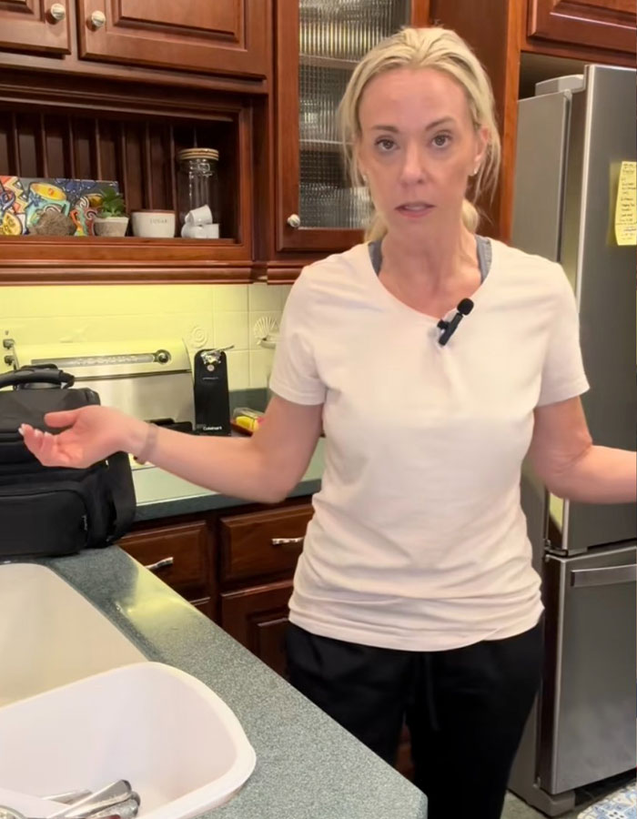 Reality star Kate Gosselin in a kitchen, wearing a white shirt, appearing concerned during a candid moment at home.
