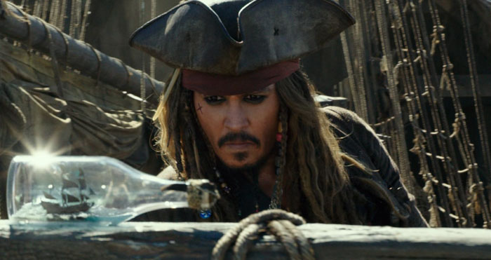 Johnny Depp as Jack Sparrow on a ship deck, focused on a bottle with a miniature ship inside, sea and rigging in background.