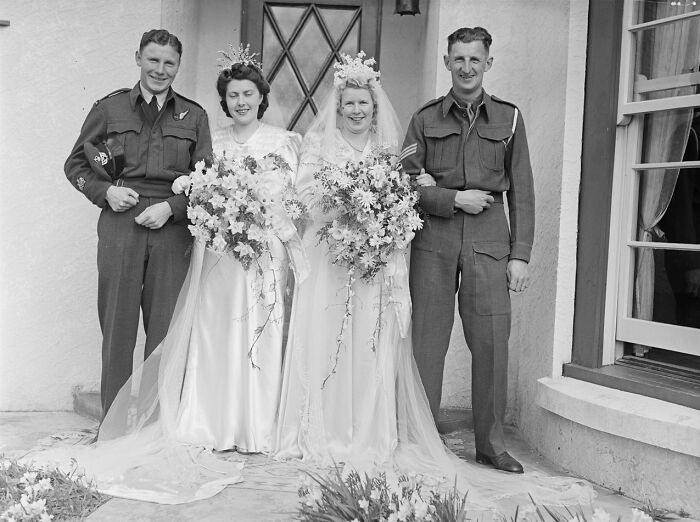 Two 1940s brides in wedding gowns with floral bouquets standing beside two soldiers in uniform, capturing love in war.