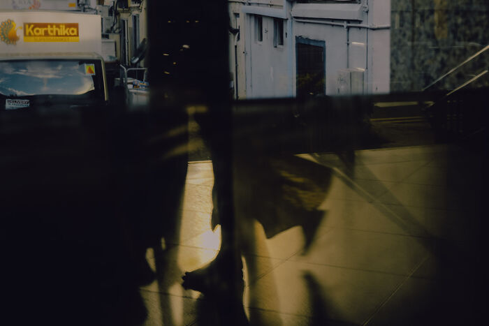 Abstract cinematic image capturing ordinary moments with shadowy reflections and soft warm lighting in an urban setting by a photographer.