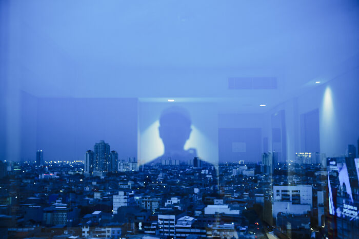 Shadowy photographer reflection over a cityscape at dusk capturing poetic cinematic moments through a window pane.