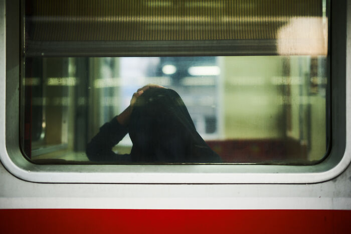 Person in a hoodie seen through a train window, capturing an ordinary moment turned poetic and cinematic by a photographer.