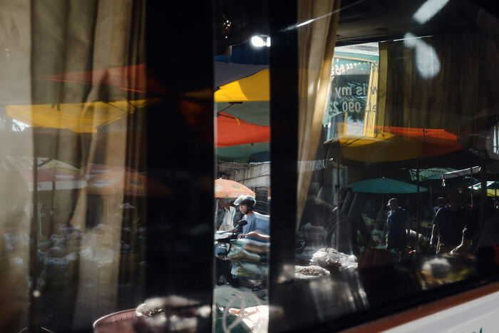 Cinematic image showing a market scene with colorful umbrellas and a person wearing a helmet on a motorcycle.