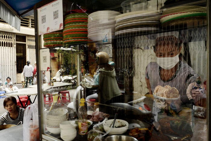 Street food vendor wearing a mask preparing food, captured in a poetic cinematic image of ordinary daily moments.