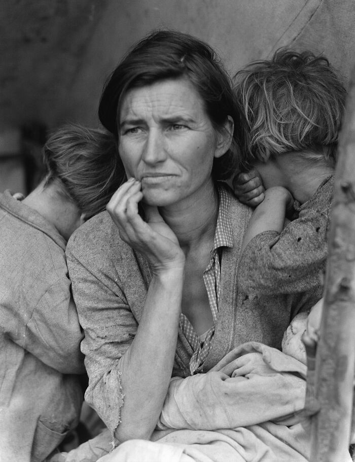 Depressed mother with her two children in worn clothing, capturing the tragedy of the 20th century during hard times.