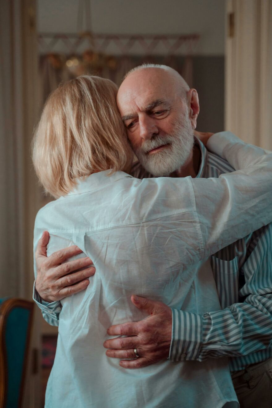 Elderly couple hugging emotionally in a home setting, illustrating relationship dynamics and gender gap issues.