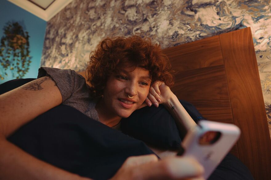 Person with curly hair lying on bed, looking at phone, illustrating latest data on men cheating and closing gender gap trends.