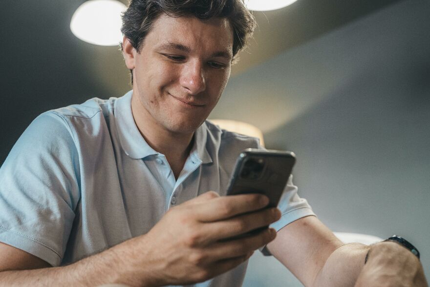 Man in a light blue shirt smiling while looking at phone, illustrating data on men cheating and closing gender gap.