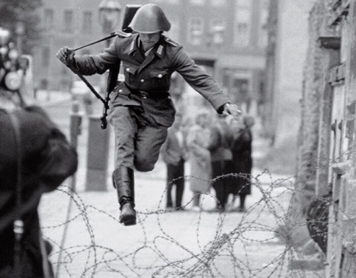 Black and white photo of a soldier jumping barbed wire, symbolizing key moments in 20th century history and conflict.