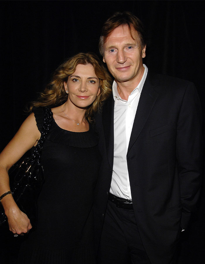 Liam Neeson and a woman posing together at an event, dressed in black and white formal attire. - 2