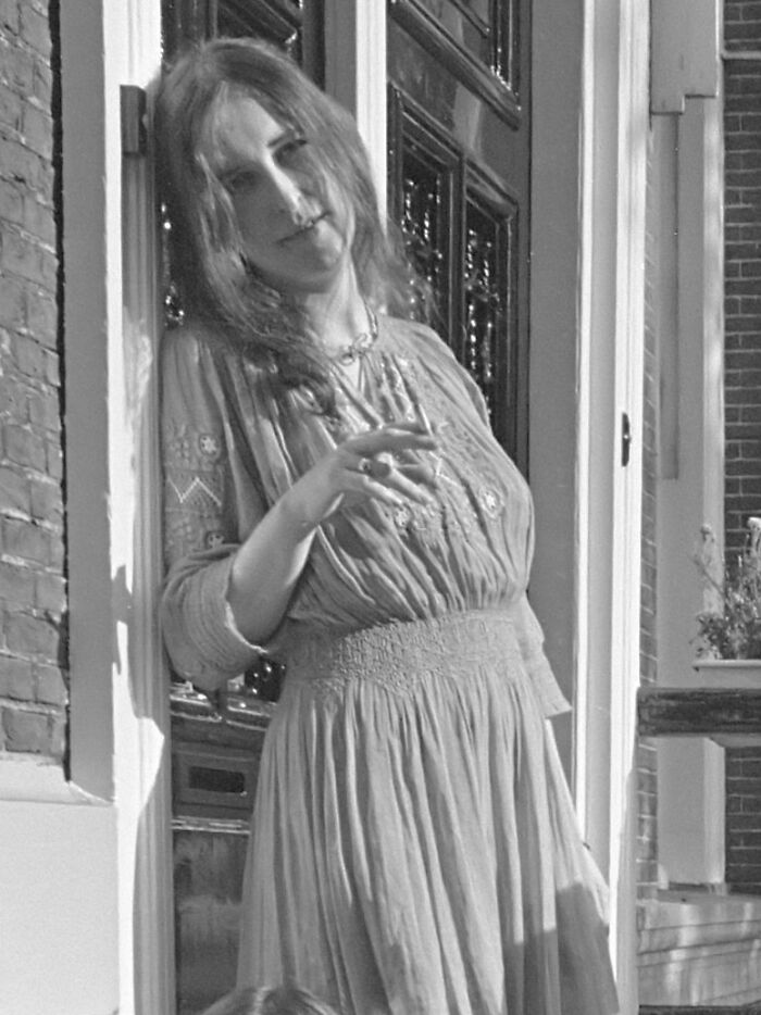Black and white photo of a woman in a vintage dress leaning against a doorframe representing 90s chilling disappearances.