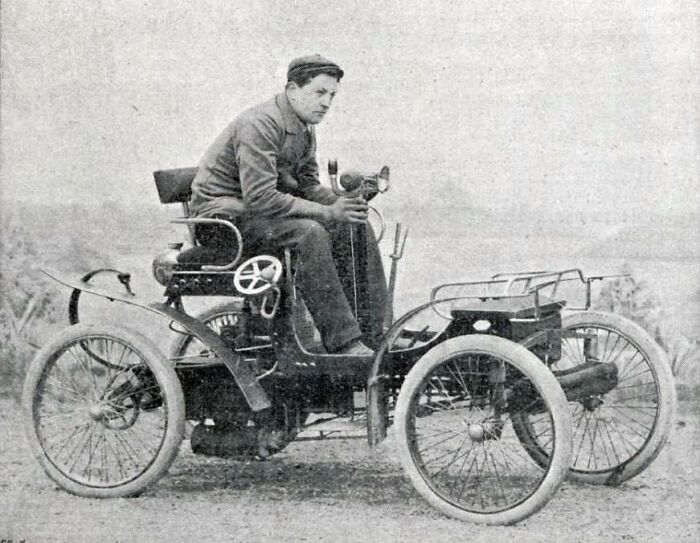 Man sitting on an early vintage car, showcasing the wild design of the first cars from 100 years ago.