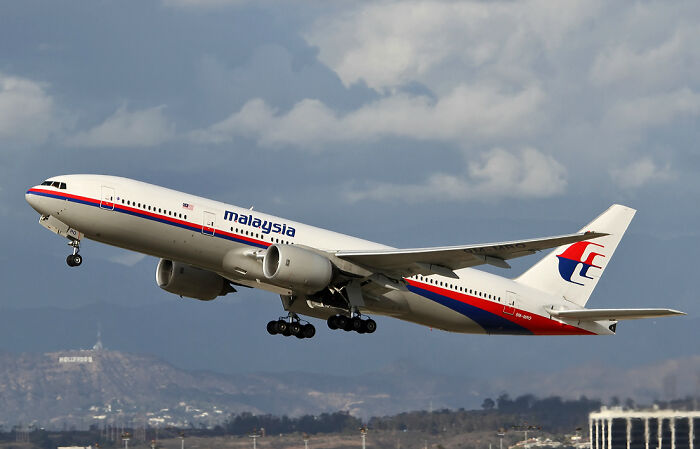 Malaysia Airlines plane taking off with cloudy sky and distant cityscape, related to unsolved mysteries keyword.