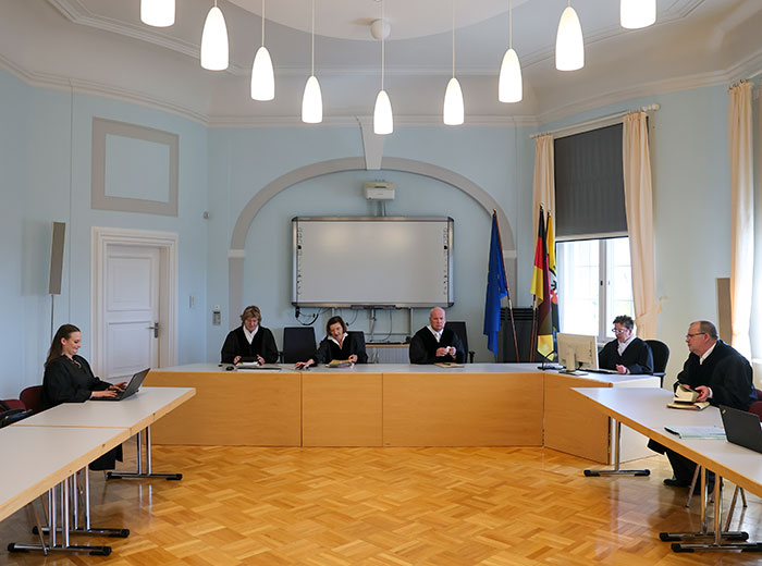 Courtroom scene with legal professionals discussing radical right-winger gender change after conviction for jail sentence placement.