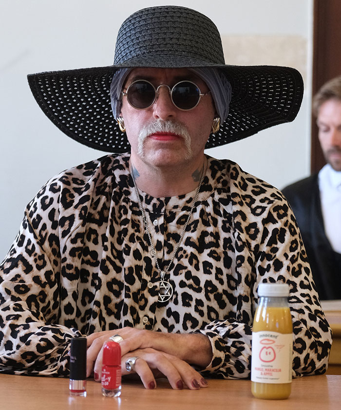 Person in leopard print shirt, wide black hat, and sunglasses, showcasing radical right-winger gender change after conviction.