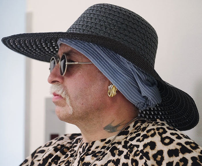 Person with a mustache wearing a wide-brimmed hat and leopard print top, representing radical right-winger gender change story