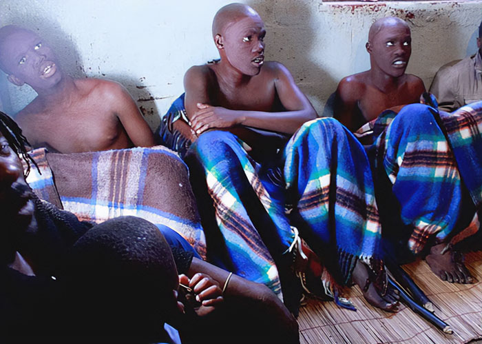 Group of young boys wrapped in blankets sitting closely together after a mass circumcision ceremony with many injured victims - 3